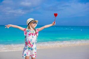 Little happy girl with red heart in hands on a tropical beach photo