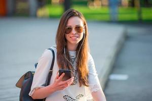 Tourist girl listening music by smartphone on summer holidays. Young attractive tourist with mobile phone outdoors enjoying holidays travel destination in tourism and exploring concept photo