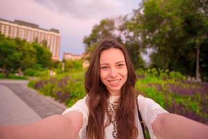 joven caucásica haciendo selfie en el fondo de las atracciones al aire libre. niña feliz disfruta de su fin de semana en la ciudad europea foto