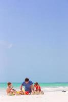 Father and kids making sand castle at tropical beach photo