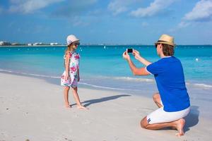 padre joven haciendo una foto en el teléfono de una niña en la playa