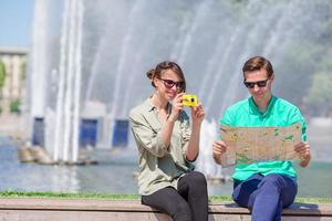 Young tourist friends traveling on holidays in Europe smiling happy. Girl taking photos in the park and man with city map in search of attractions