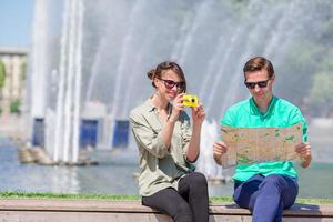 jóvenes amigos turistas que viajan de vacaciones en europa sonriendo felices. chica tomando fotos en el parque y hombre con mapa de la ciudad en busca de atracciones