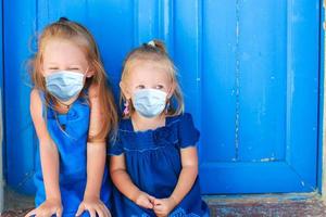 Closeup of Little adorable girls sitting near old blue door in Greek village, Emporio, Santorini photo