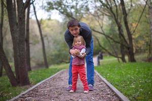 Little girl with young dad in the park at warm autumn day photo