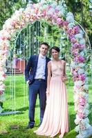 encantadora pareja joven en un arco de flores en la ceremonia de la boda foto