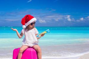 Little girl at Santa hat sitting on a large suitcase with map in hands photo