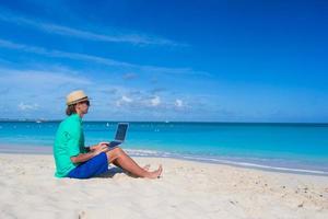 joven trabajando en la computadora portátil en la playa tropical foto