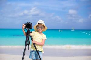 Portrait of little girl with camera on a tripod at white sandy beach photo