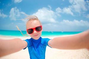 niña adorable que hace el selfie en la playa blanca tropical foto