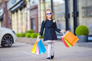 Adorable little girl walking with shopping bags outdoors photo