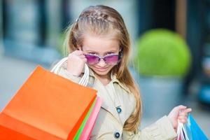 Portrait of adorable little girl walking with shopping bags outdoors photo