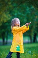 Adorable toddler girl wearing waterproof coat playing outdoors by rainy and sunny day photo