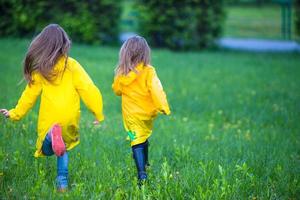 Funny cute toddler girls wearing waterproof coat playing outdoors by rainy and sunny day photo