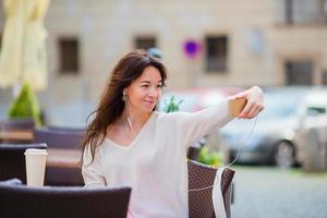 joven mujer caucásica enviando un mensaje y tomando un autorretrato en un café al aire libre. niña feliz disfruta del verano en vacaciones en europa foto