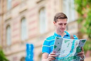 Young man in sunglasses with a city map and backpack in Europe. Caucasian tourist looking at the map of European city in search of attractions. photo