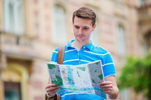 Man tourist with a city map and backpack in Europe. Caucasian boy looking at the map of European city in search of attractions. photo