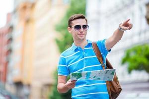 Man tourist with a city map and backpack in Europe. Caucasian boy looking at the map of European city in search of attractions. photo