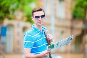 Young man in sunglasses with a city map and backpack in Europe. Caucasian tourist looking at the map of European city in search of attractions. photo