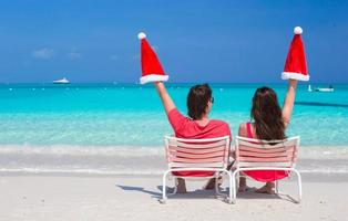 Happy young couple in red Santa Hats sitting on beach chairs photo