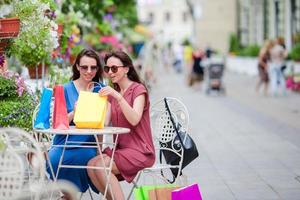 dos compradores coloridos de moda con bolsas de compras con un teléfono inteligente en la calle. concepto de venta, consumismo y personas. las chicas caucásicas disfrutan de su cálido día en un café al aire libre.