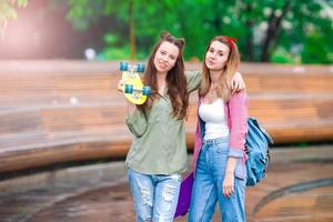 dos chicas hipster con monopatín al aire libre a la luz del atardecer. mujeres deportivas activas divirtiéndose juntas en el parque de patinaje. foto