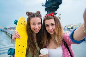 Two hipster girls makihg selfie with skateboard outdoors in sunset light. Active sporty women having fun together in skate park. photo