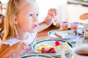 Adorable little girl having breakfast at restaurant photo