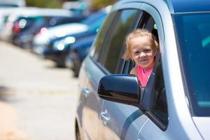 Little adorable girl in the car looking throw window at summer vacation photo