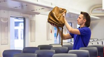 joven caucásico poniendo equipaje en el estante superior del tren foto