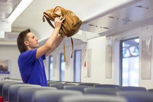 Young caucasian man putting luggage on the top shelf at aircraft photo