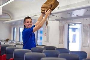 joven caucásico poniendo equipaje en el estante superior del avión foto