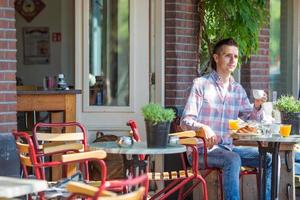 feliz joven sentado en un café al aire libre en una ciudad europea desayunando foto