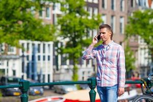Young caucasian man talking by cell phone on bridge in european city photo