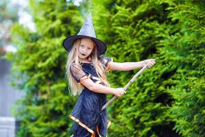 Adorable little girl wearing witch costume with broom on Halloween outdoors photo