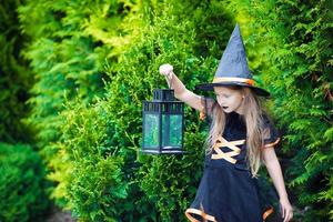 Adorable little girl wearing witch costume with broom on Halloween outdoors photo