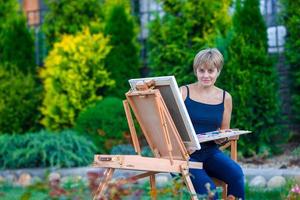 Happy woman painting a picture on an easel on a warm day photo