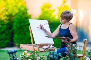 Happy woman painting a picture on an easel on a warm day photo