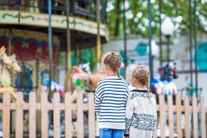 Adorable little girls near the carousel outdoors photo