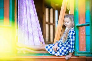 Adorable little girl in the window of rural house outdoors photo