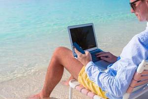 cerrar el teléfono en el fondo de la computadora en la playa foto