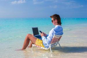 joven usando laptop en playa tropical foto