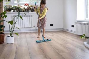 A girl dances with a mop to clean the floor in a new house - general cleaning in an empty room, the joy of moving, help with the housework