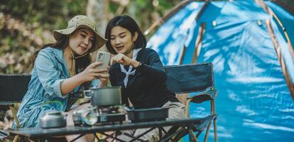 Asian pretty woman and friend use smartphone selfie on camping photo