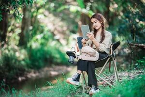 Young woman use tablet video call while camping in park photo