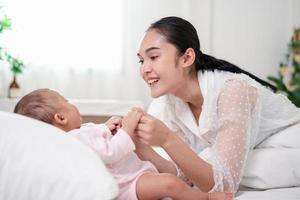 crianza de la madre y vida del nacimiento del recién nacido. mamá y bebé jugando en un dormitorio soleado, familia divirtiéndose juntos. cuidado de niños, concepto de maternidad. foto