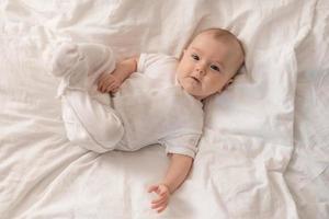 portrait of a cute baby in a white bodysuit on a bed at home with white linens. Newborn baby at home, happy motherhood. High quality photo