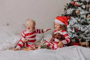 los niños en pijama rojo y blanco comen dulces navideños sentados en la cama. hermano y hermana, niño y niña comparten regalos. mañana de Navidad. estilo de vida. espacio para texto. foto de alta calidad