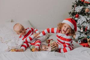 los niños en pijama rojo y blanco comen dulces navideños sentados en la cama. hermano y hermana, niño y niña comparten regalos. mañana de Navidad. estilo de vida. espacio para texto. foto de alta calidad