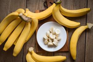 racimo de plátanos - plátano cortado en rodajas sobre fondo de madera, fruta madura de cáscara de plátano en el suelo - vista superior foto